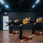 Five dancers showcase flexibility and balance in a dance studio during rehearsal.