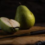 Fresh pears on a wooden board, one sliced with a knife, in a rustic setting.
