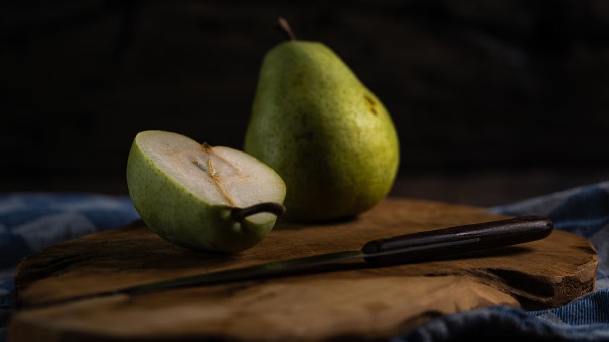 Fresh pears on a wooden board, one sliced with a knife, in a rustic setting.